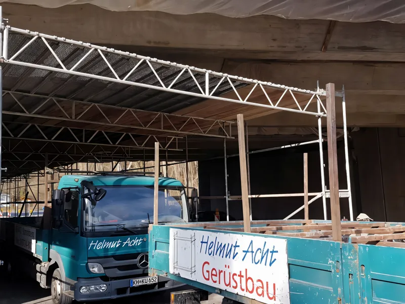 Gerüst unter einem Brückenüberbau, davor der Firmen-LKW mit Beschriftung