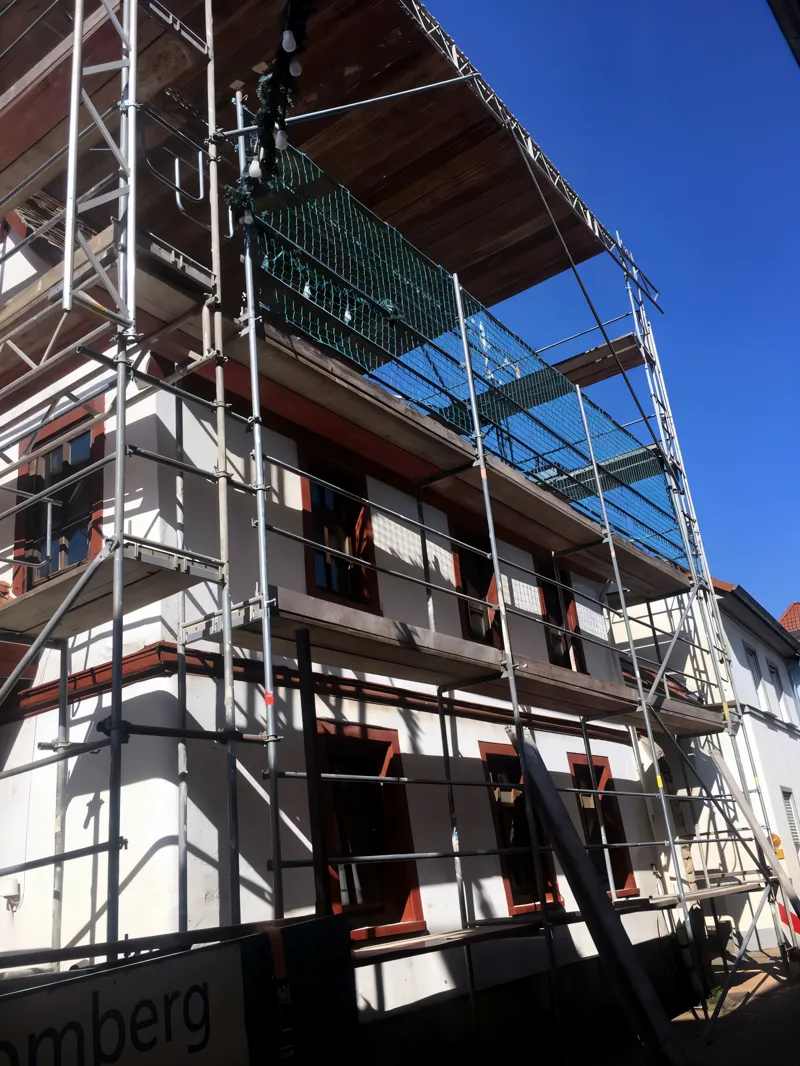 Zweigeschossiges Wohnhaus mit Gerüst über die volle Länge, grünes Schutznetz an der oberen Lage