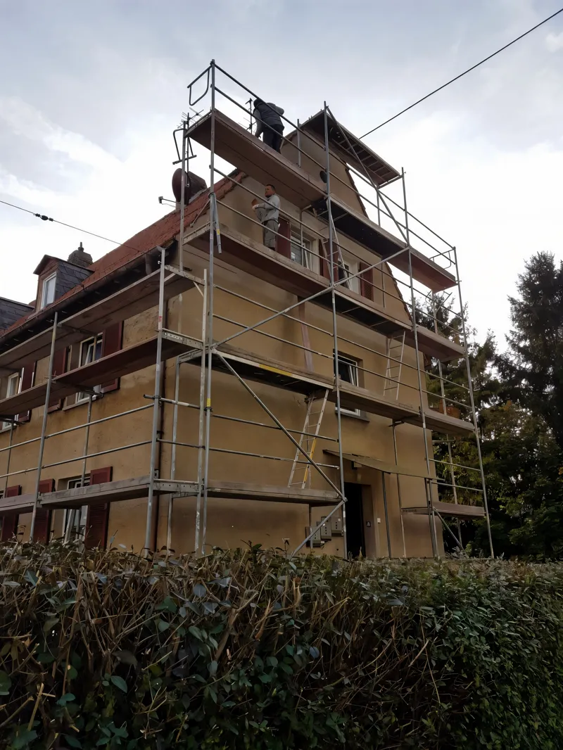 Mehrfamilienhaus mit Gerüst bis über den Giebel, Arbeiter auf der obersten Lage
