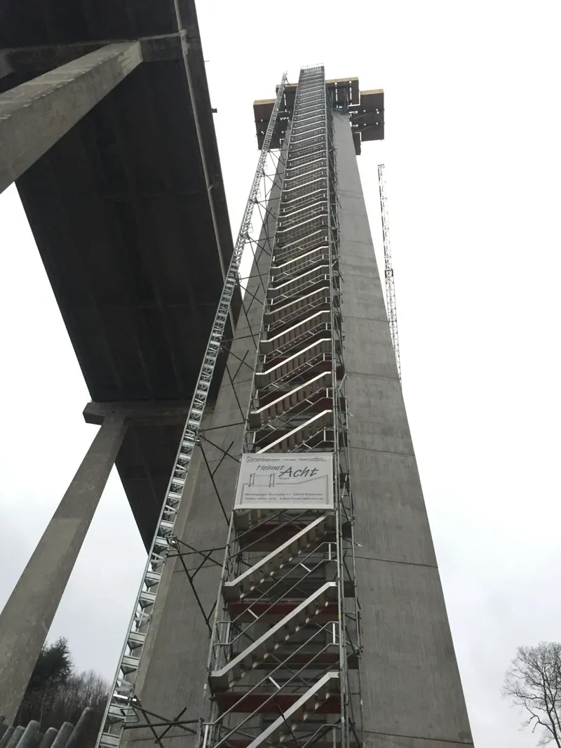 Treppenturm am Pfeiler einer Talbrücke, über die volle Höhe, mit Firmenbanner von Gerüstbau Acht