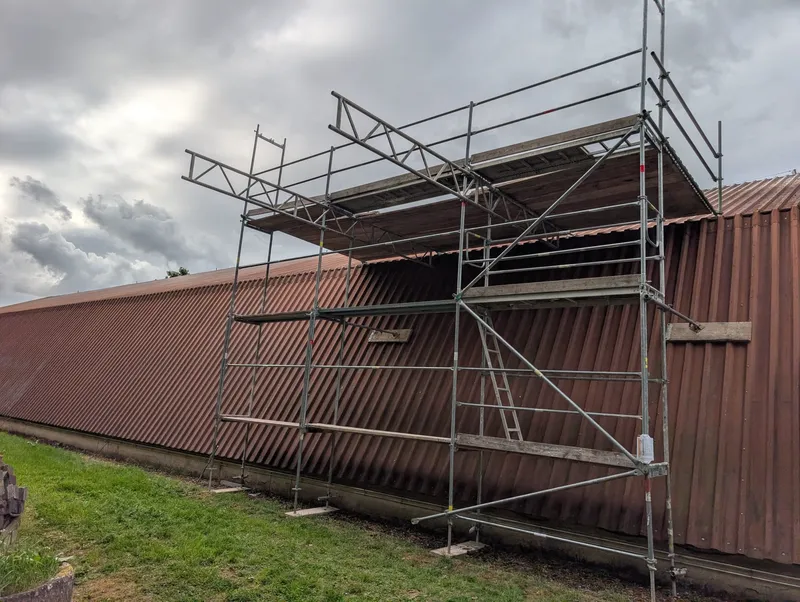 Arbeitsgerüst mit Gitterträgern an der Traufe einer Halle mit rostbraunem Wellblechdach