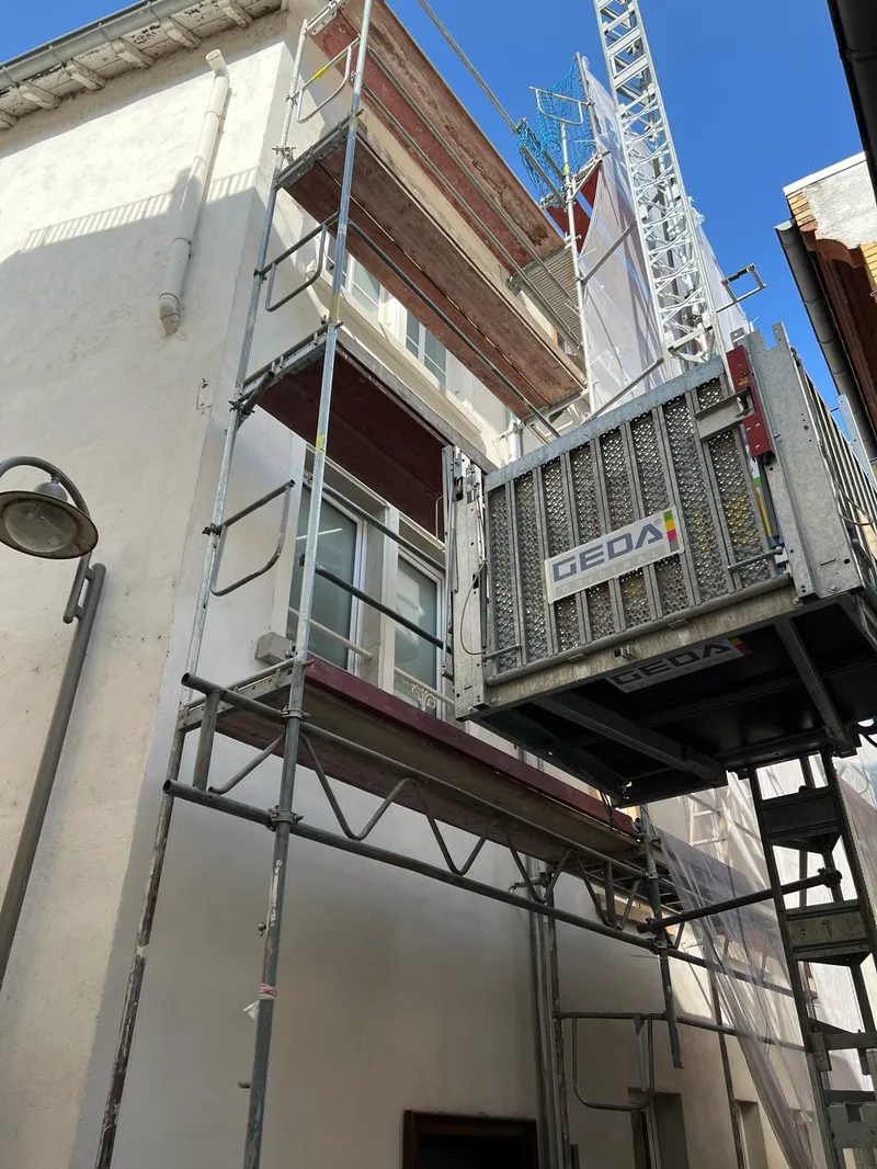 Altbau in enger Gasse, Gerüst mit Bauaufzug GEDA, darüber blaues Fangnetz