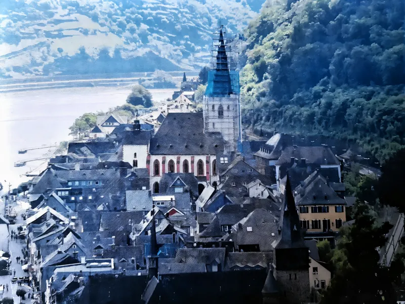 Blick über die Dächer eines Rheinorts auf die eingerüstete Kirche