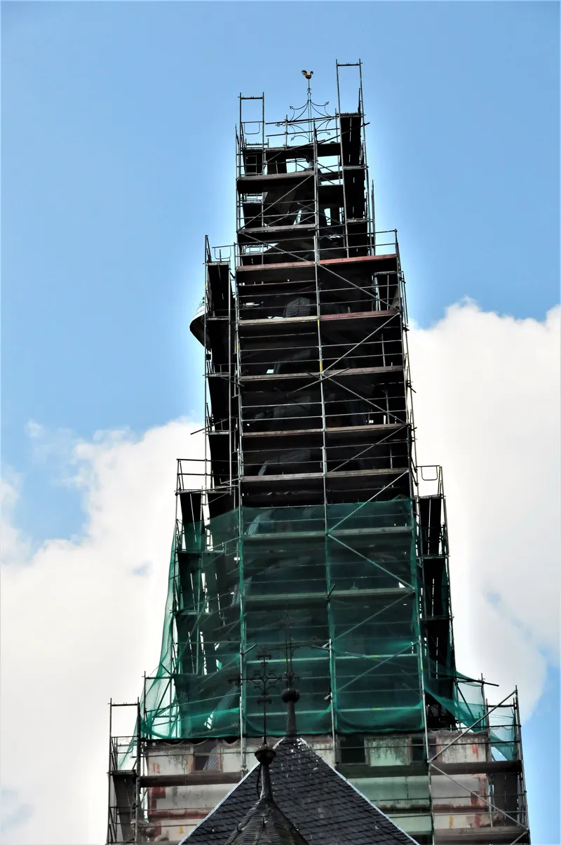 Kirchturm mit grünem Schutznetz, eingerüstet über das Dach des Langhauses hinaus