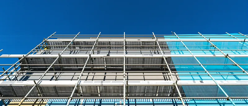 Blick senkrecht nach oben an einer eingerüsteten Fassade, die Ständer laufen auf den blauen Himmel zu