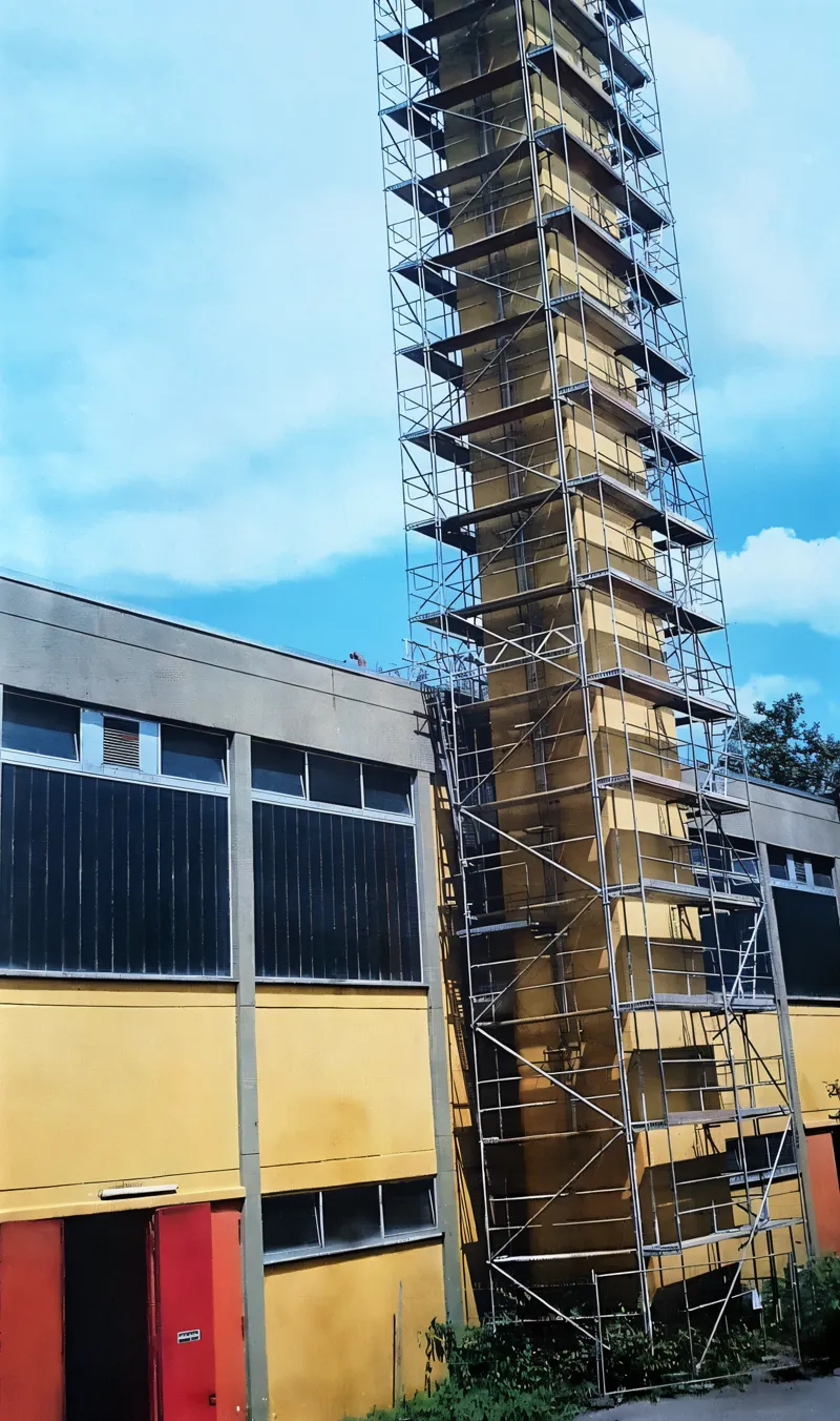 Schmaler Turm an einer Halle, über die volle Höhe eingerüstet